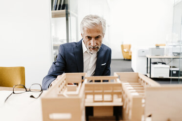 Mature businessman examining architectural model in office - KNSF02148