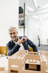 Porträt eines lächelnden reifen Geschäftsmannes mit Architekturmodell im Büro - KNSF02149