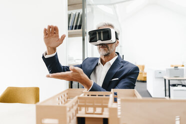 Mature businessman with architectural model in office wearing VR glasses - KNSF02154