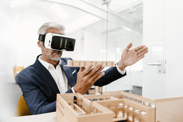 Mature businessman with architectural model in office wearing VR glasses - KNSF02158