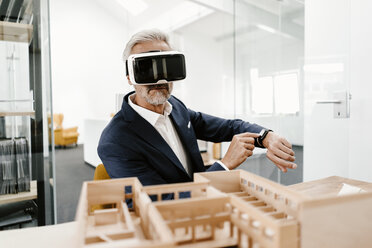 Mature businessman with architectural model in office wearing VR glasses - KNSF02160