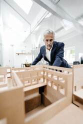 Mature businessman examining architectural model in office - KNSF02170