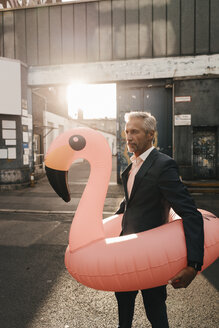 Mature businessman on the street with inflatable flamingo - KNSF02179