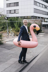 Älterer Geschäftsmann auf der Straße mit aufblasbarem Flamingo - KNSF02182