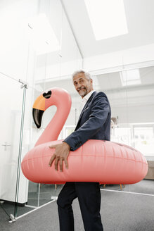 Businessman in office with inflatable flamingo - KNSF02190