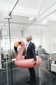 Businessman in office with inflatable flamingo - KNSF02191