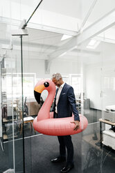 Glücklicher Geschäftsmann im Büro mit aufblasbarem Flamingo - KNSF02192