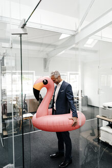 Happy businessman in office with inflatable flamingo - KNSF02192