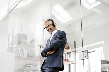 Happy mature businessman in office wearing headphones - KNSF02208
