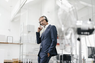 Mature businessman in office wearing headphones - KNSF02209