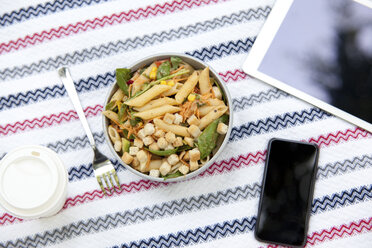 Cell phone, tablet, coffee to go and a bowl of noodle salad on blanket in a park - MFRF00916