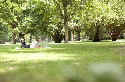 Man lying on blanket in a park using laptop - MFRF00933