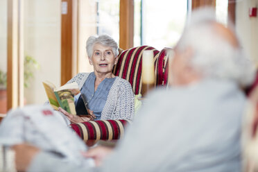 Senior man and woman sitting in library, reading book and newspaper - ZEF14204