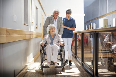 Gereatric nurse helping senior man and woman to walk down corridor - ZEF14221