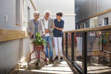 Altenpflegerin hilft älterem Mann und älterer Frau beim Gehen im Flur - ZEF14224