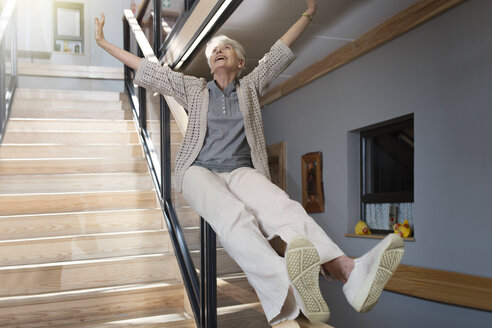 Happy senior woman sliding down a staircase - ZEF14227