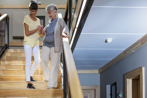 Krankenschwester hilft einer älteren Frau die Treppe hinunter, lizenzfreies Stockfoto