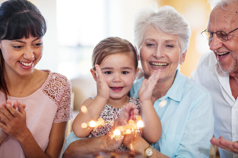 Little girl lwatching sparklers on a birthday cake, sitting on grandmother's lap stock photo