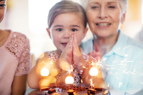 Little girl lwatching sparklers on a birthday cake, sitting on grandmother's lap stock photo