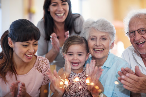 Little girl lwatching sparklers on a birthday cake, sitting on grandmother's lap, with family around stock photo