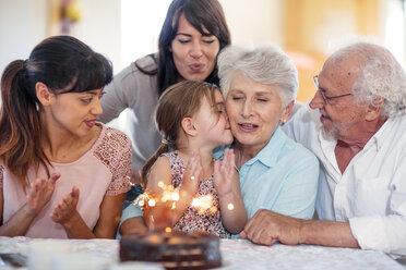 Kleines Mädchen beobachtet Wunderkerzen auf einer Geburtstagstorte, auf dem Schoß der Großmutter sitzend, mit der Familie um sich herum - ZEF14254