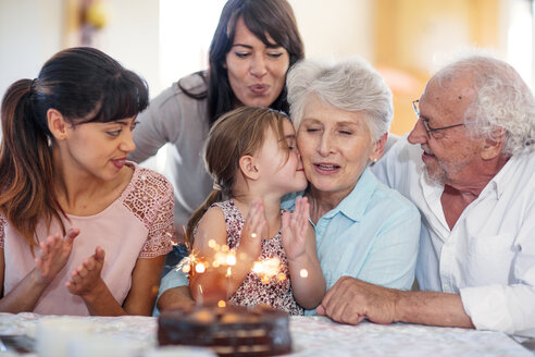 Little girl lwatching sparklers on a birthday cake, sitting on grandmother's lap, with family around - ZEF14254