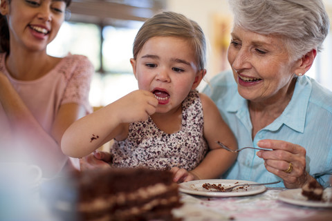 Großeltern feiern mit ihrer Enkelin einen Geburtstag und essen Schokoladenkuchen, lizenzfreies Stockfoto