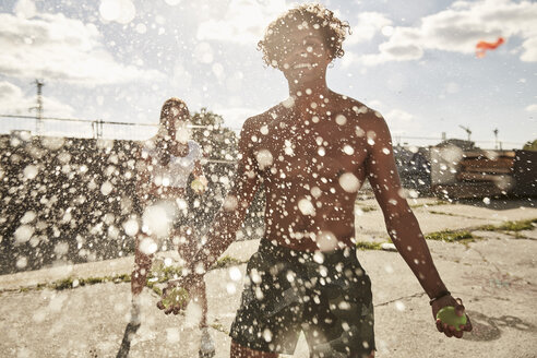 Young couple throwing water bags in summer - SUF00260