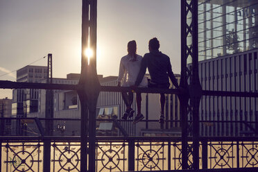 Deutschland, München, Junges Paar sitzt auf Brücke und genießt Sonnenuntergang - SUF00261