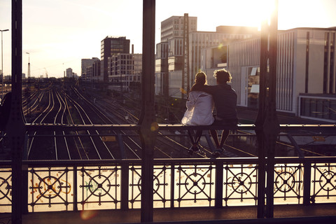 Germany, Munich, Young couple sitting on bridge, enjoying sunset stock photo