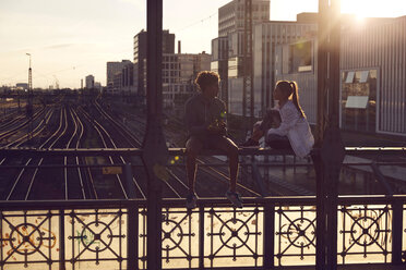 Germany, Munich, Young couple sitting on bridge, enjoying sunset - SUF00264