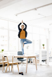 Businesswoman practising yoga on desk in a loft - KNSF02231