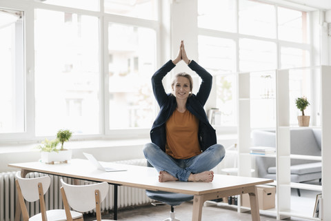 Geschäftsfrau übt Yoga am Schreibtisch in einem Loft, lizenzfreies Stockfoto