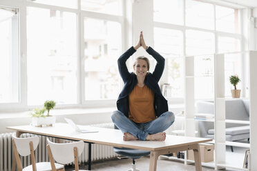 Businesswoman practising yoga on desk in a loft - KNSF02239