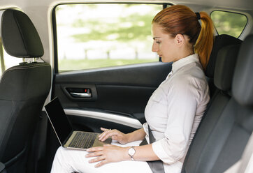Geschäftsfrau auf der Rückbank eines Autos sitzend, Laptop benutzend - MOMF00185