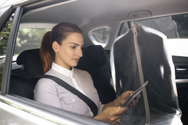 Businesswoman sitting on backseat of a car using tablet - MOMF00187