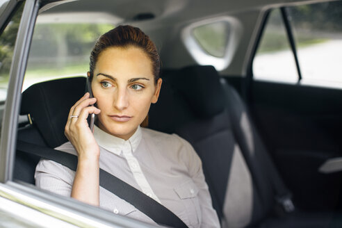 Geschäftsfrau am Telefon auf der Rückbank eines Autos sitzend - MOMF00190