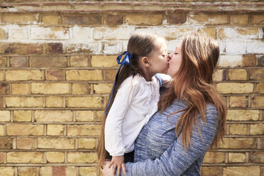 Mutter küsst ihre kleine Tochter vor einer Backsteinmauer - IGGF00007