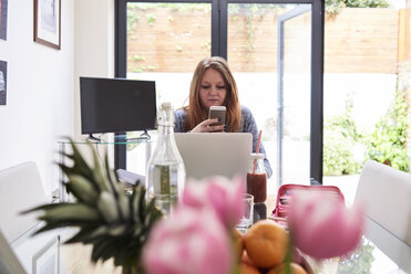 Portrait of woman using cell phone at table in the living room - IGGF00015