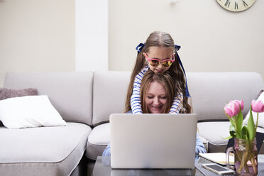 Portrait of smiling mother and little daughter using laptop in the living room - IGGF00019