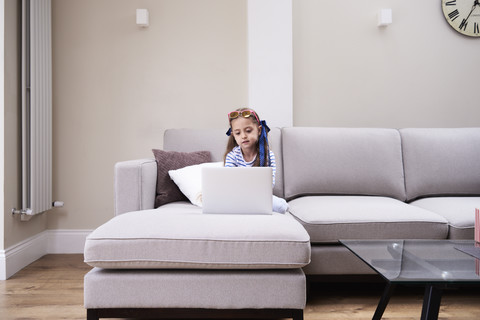 Little girl sitting on the couch looking at laptop stock photo