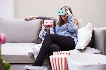 Mutter und kleine Tochter sitzen auf der Couch und haben Spaß mit einer Virtual-Reality-Brille - IGGF00023