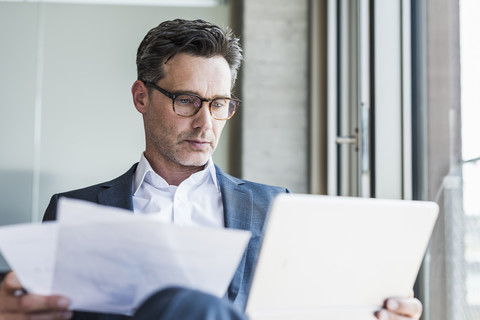 Porträt eines seriösen Geschäftsmannes mit Dokumenten, der auf ein Tablet schaut, lizenzfreies Stockfoto