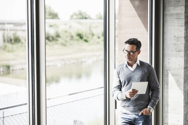 Nachdenklicher Geschäftsmann mit Tablet und Blick durch das Fenster - UUF11244