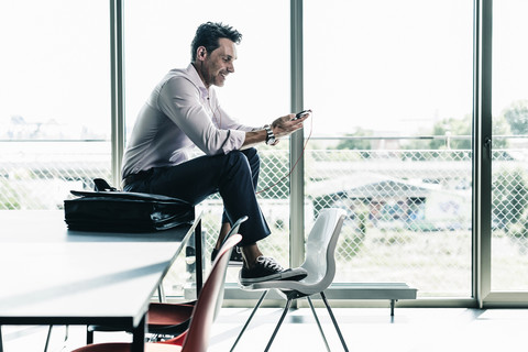 Geschäftsmann im Büro, der auf dem Schreibtisch sitzt und ein Smartphone benutzt, lizenzfreies Stockfoto