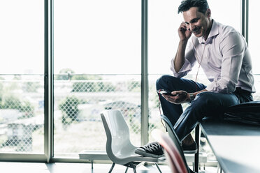 Geschäftsmann im Büro, der auf dem Schreibtisch sitzt und ein Smartphone benutzt - UUF11258