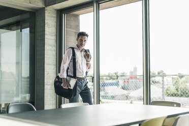 Businessman standing by window, entering the office - UUF11261