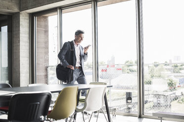 businessman standing by window, making a phone call - UUF11262