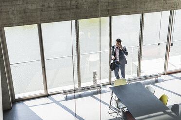 businessman standing by window, making a phone call - UUF11267