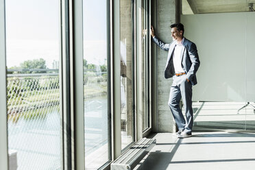 Businessman standing by window, with hands in pockets - UUF11273